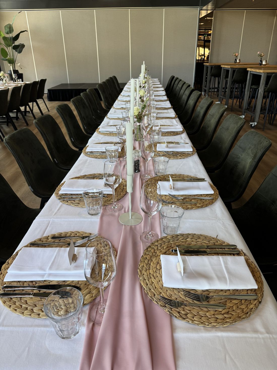 Lange gedekte tafel binnen met roze loper en rieten placemats
